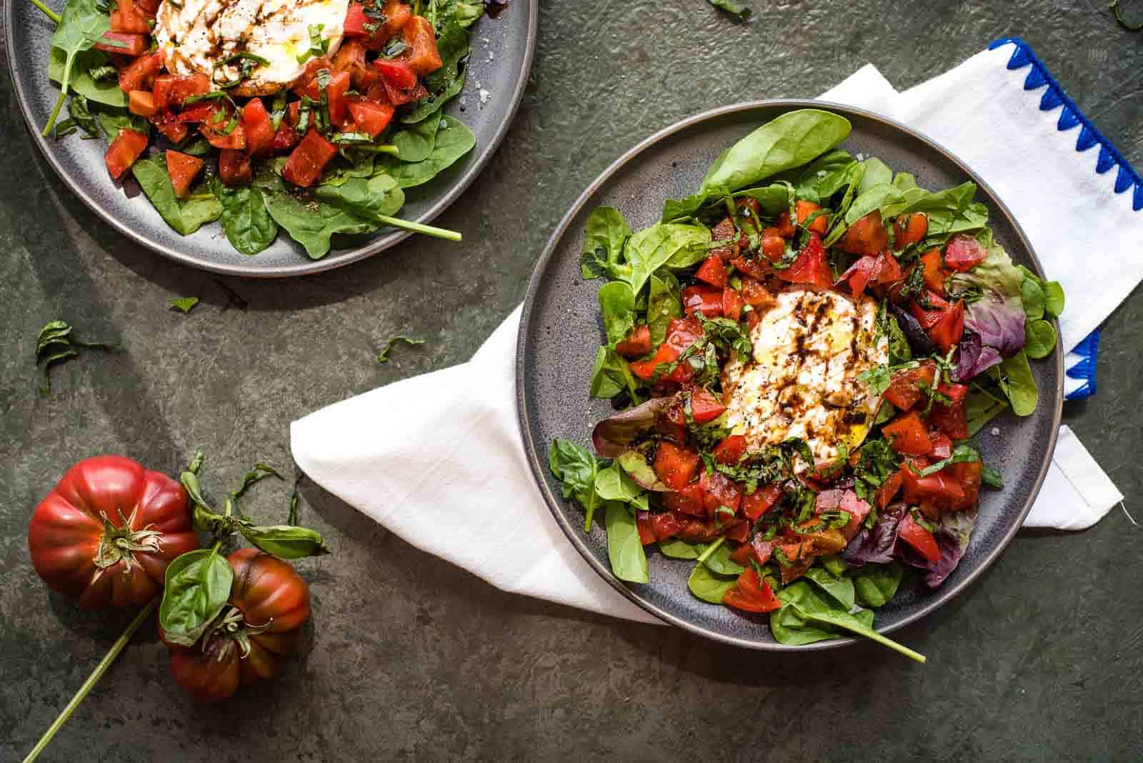 Two plates of cheesy salad with tomatoes and goat cheese.