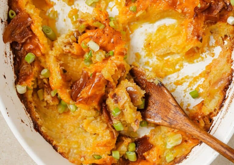 Cheesy potato casserole in a white dish with a wooden spoon.