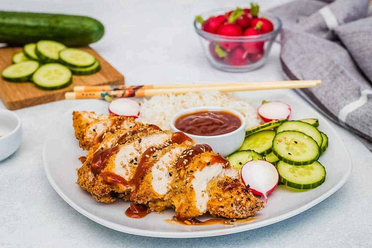 Air fryer chicken katsu topped with katsu sauce on a plate with rice and cucumbers.