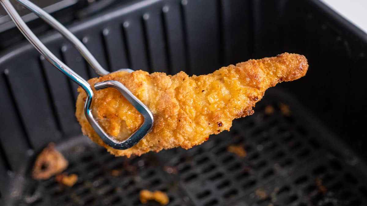 A piece of chicken being pulled out of an air fryer.