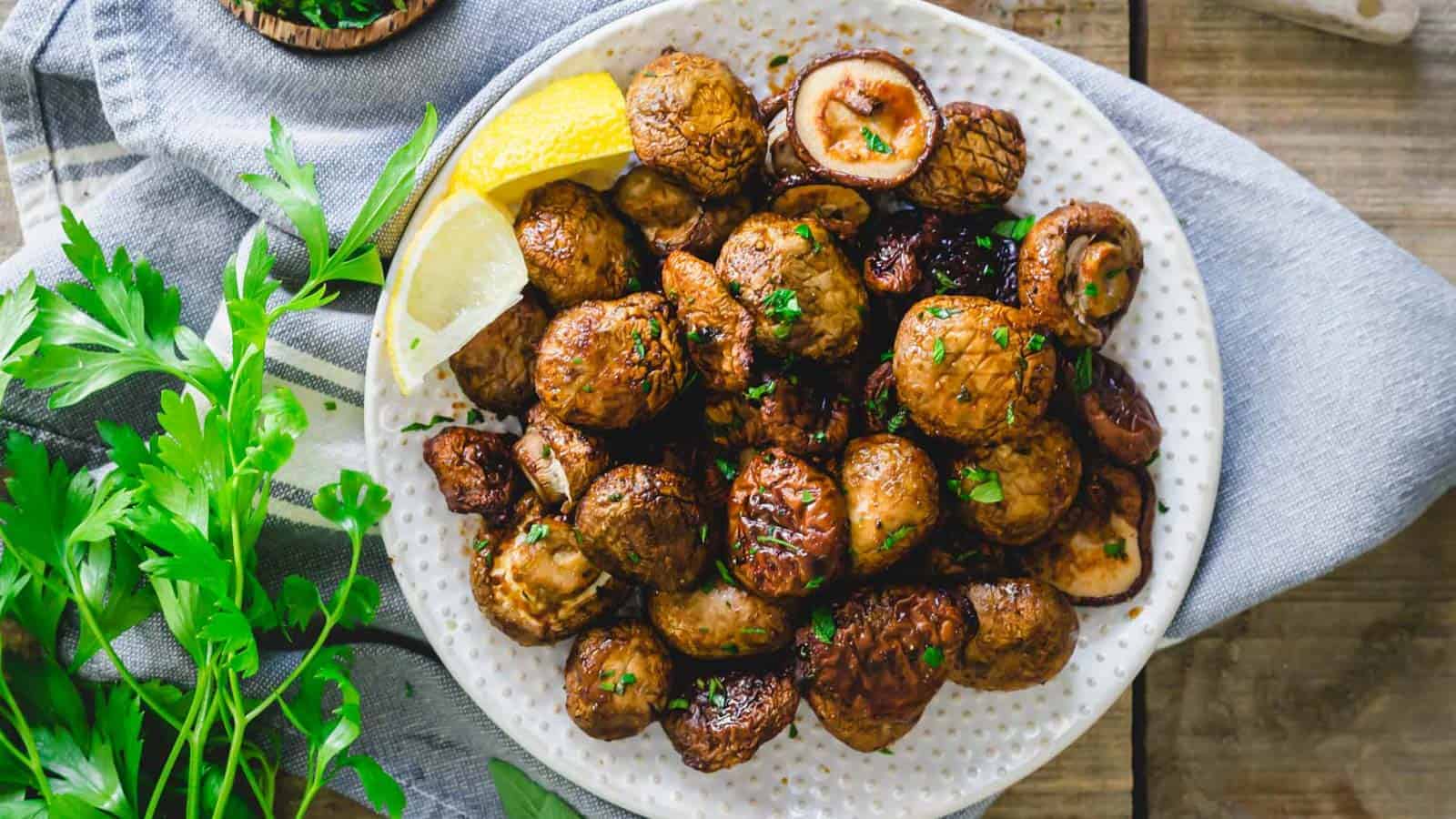 Air fryer shiitake and cremini mushrooms on a plate with lemon wedges.