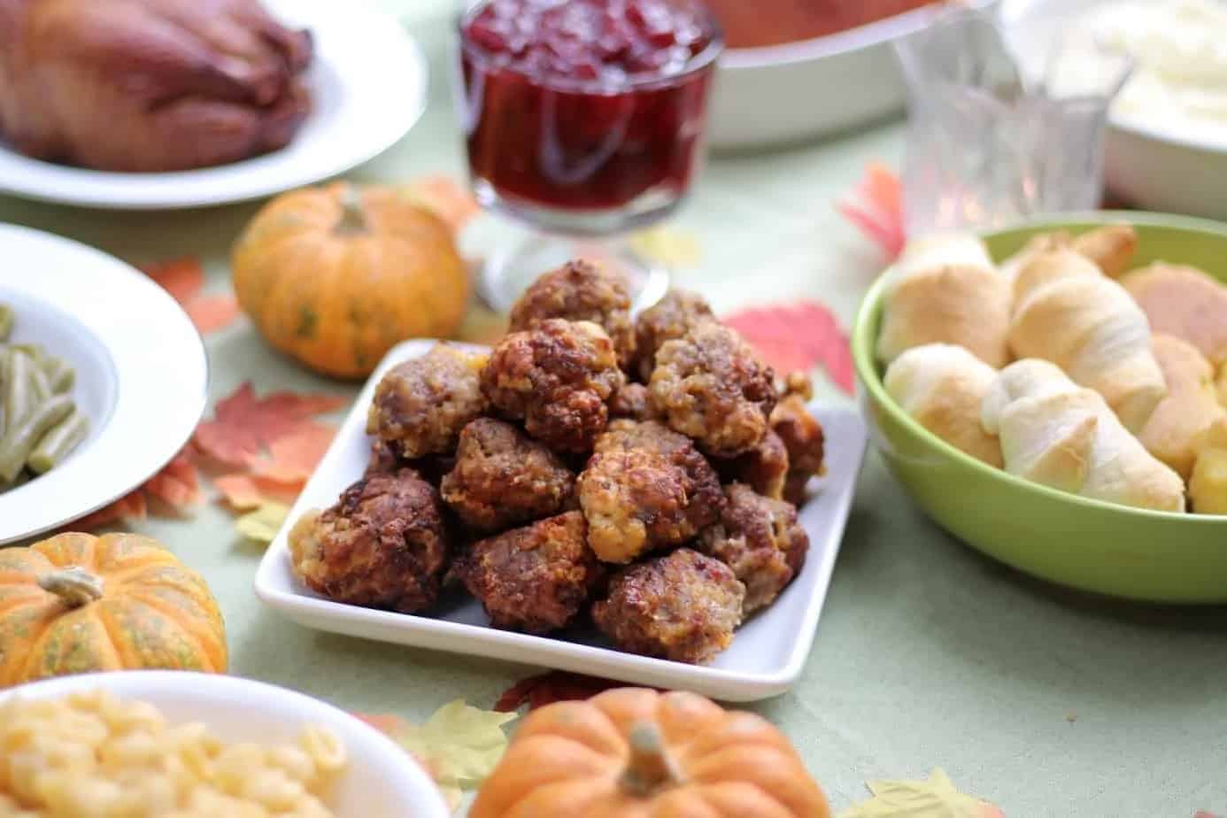 Stack of sausage balls on a square white plate, in a Thanksgiving table spread.