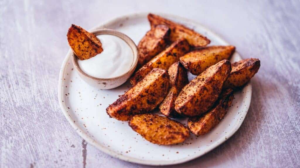 Fried potato wedges on a plate with dipping sauce.