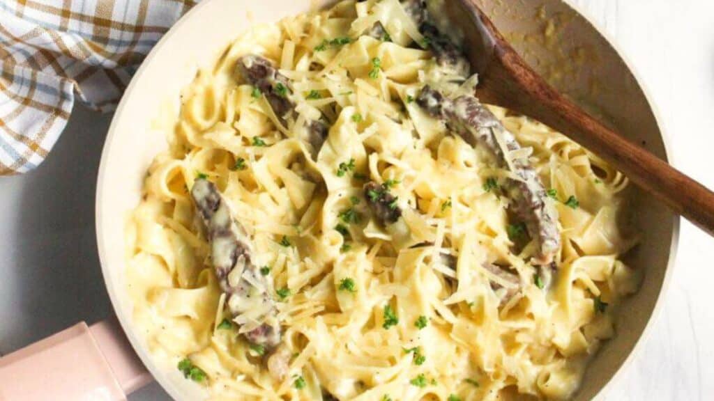 A pan full of pasta and sauce with a wooden spoon.