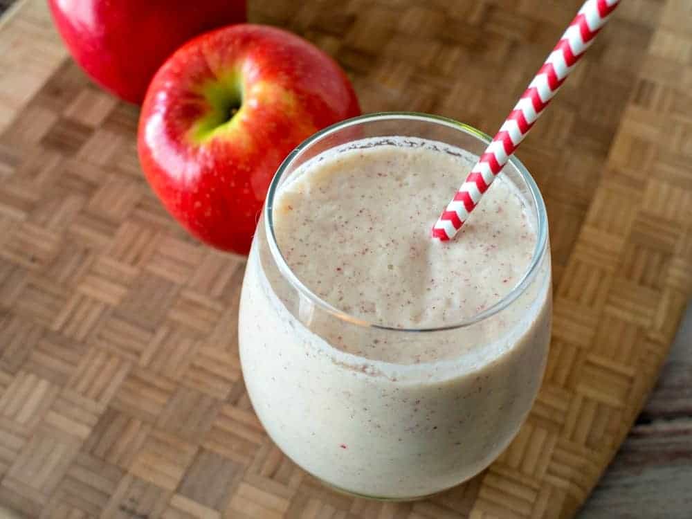 Apple smoothie in a glass with a red polka dot straw on a cutting board.