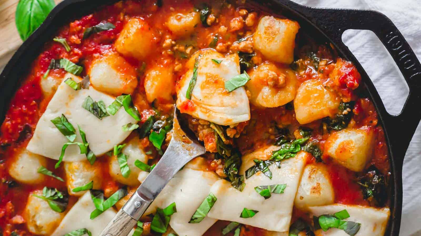 Gnocchi with ground pork, tomatoes, mozzarella and spinach in a cast iron skillet.