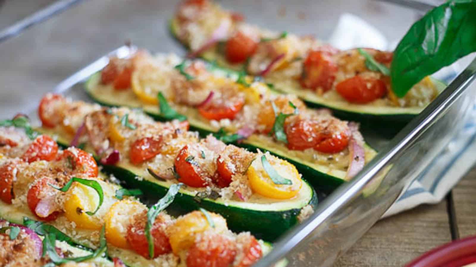 Bruschetta hummus stuffed zucchini boats in a glass baking dish.