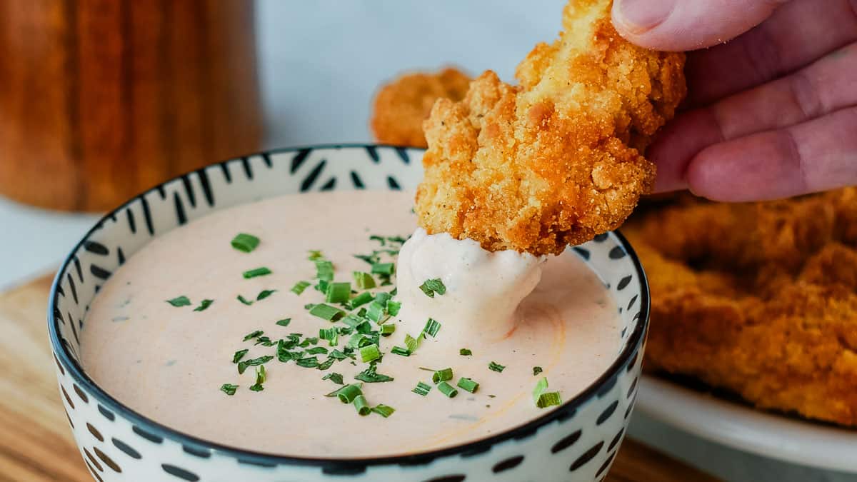 A person dipping a chicken wing dip into a bowl.