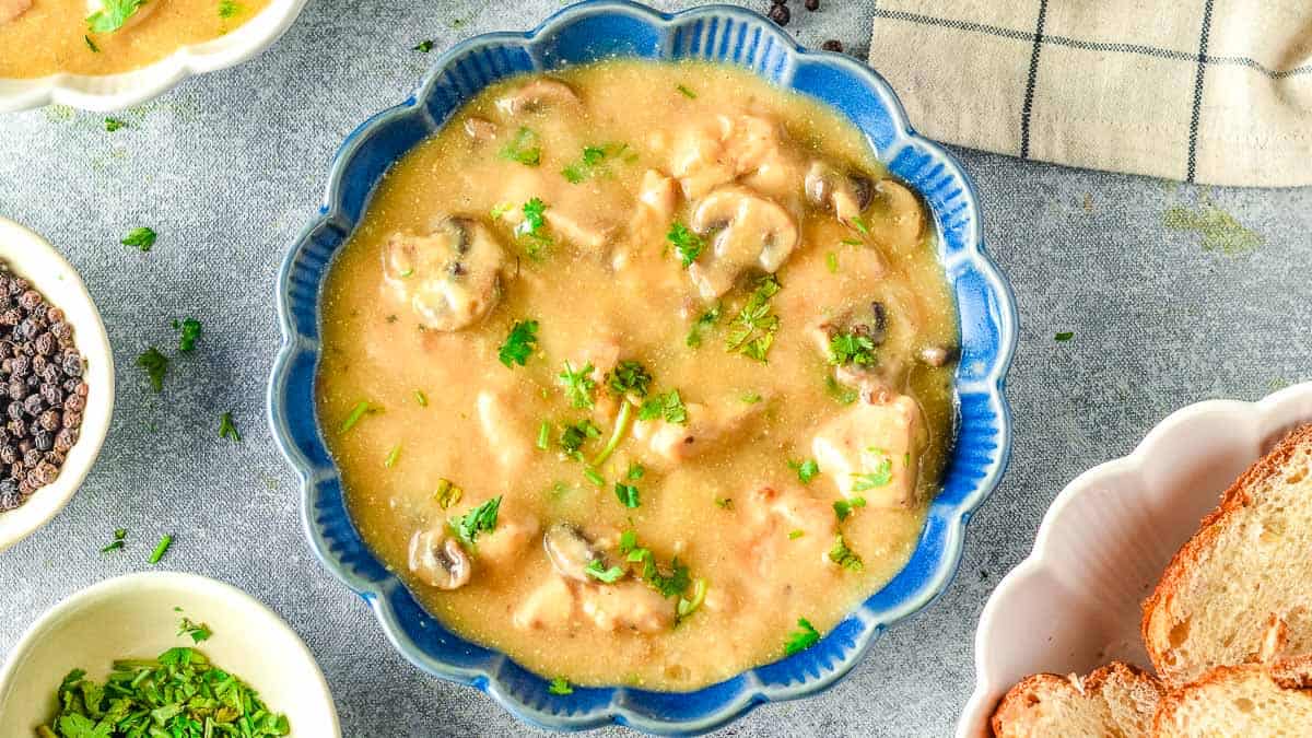 A bowl of chicken stroganoff with bread and parsley.