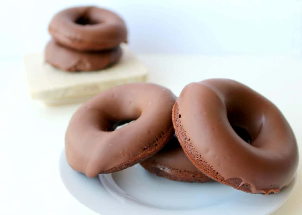 Three chocolate glazed donuts on a plate.