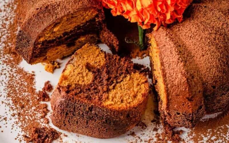 A chocolate bundt cake with orange flowers on a plate.