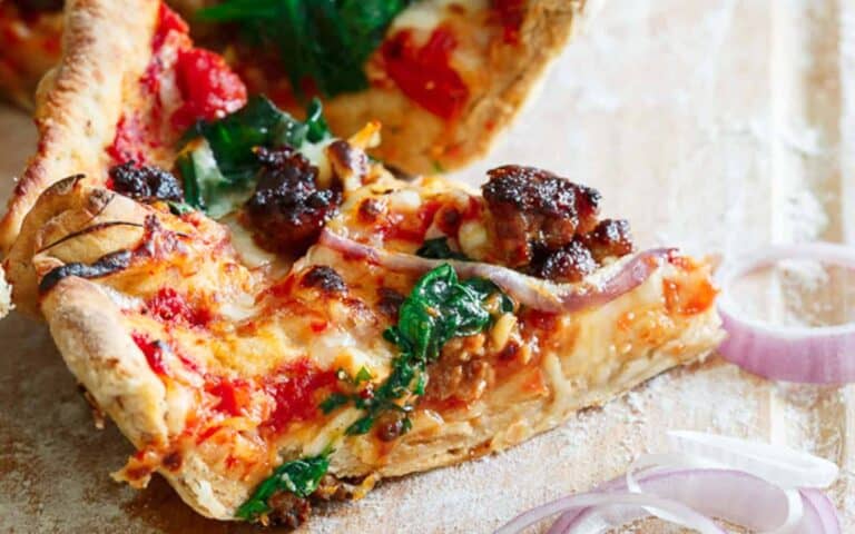 A slice of pizza with mushrooms and spinach on a cutting board.