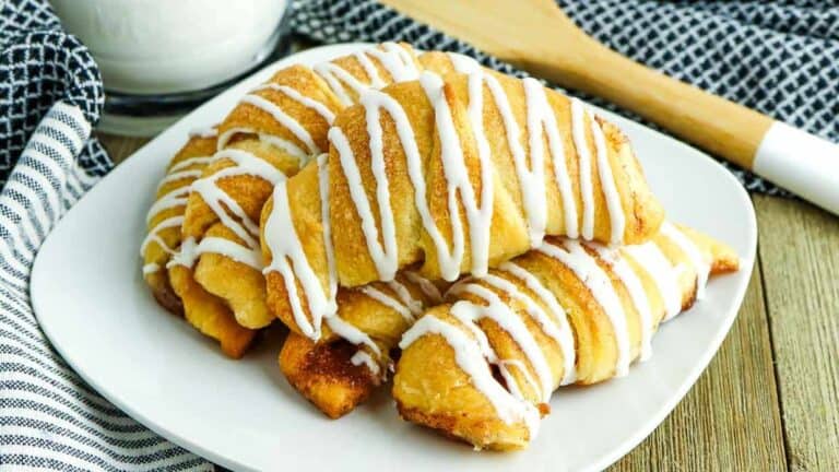 A plate of cinnamon roll pastries with icing and a glass of milk.