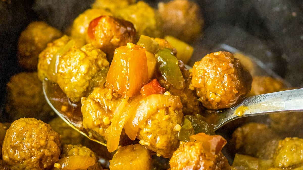 A spoonful of meatballs and vegetables in a pot.