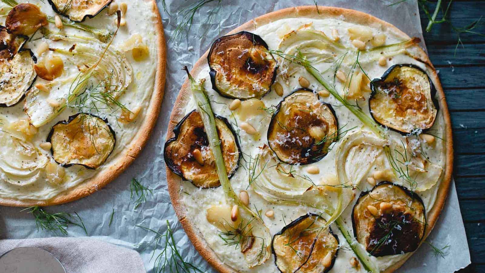 Two eggplant feta pizzas with fennel and garlic on parchment paper.