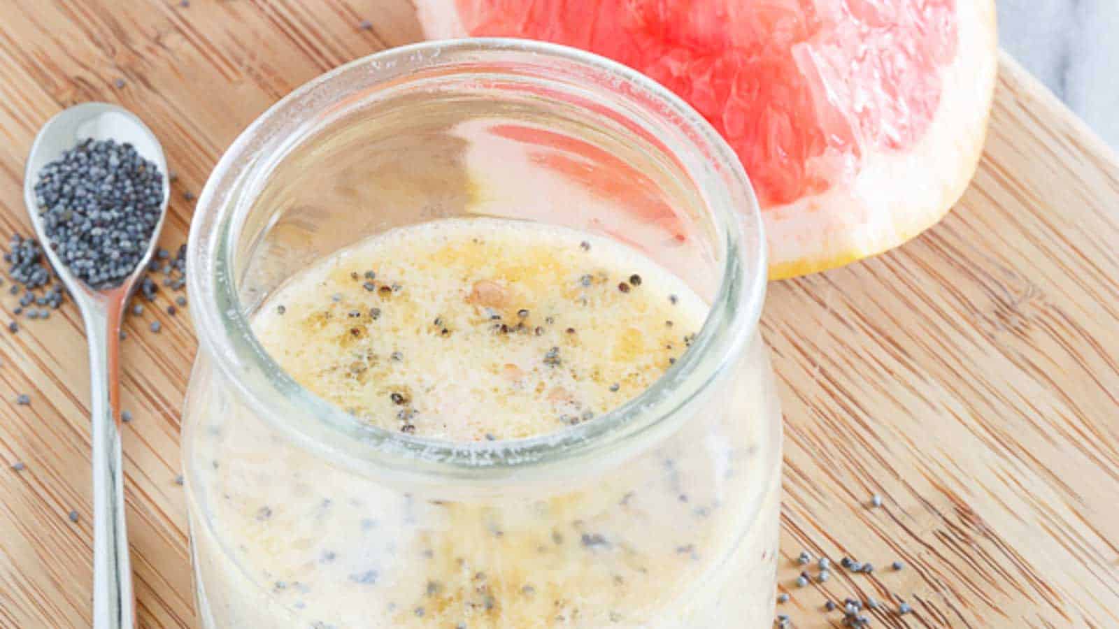 A glass of grapefruit dressing with poppyseeds seeds and a spoon.