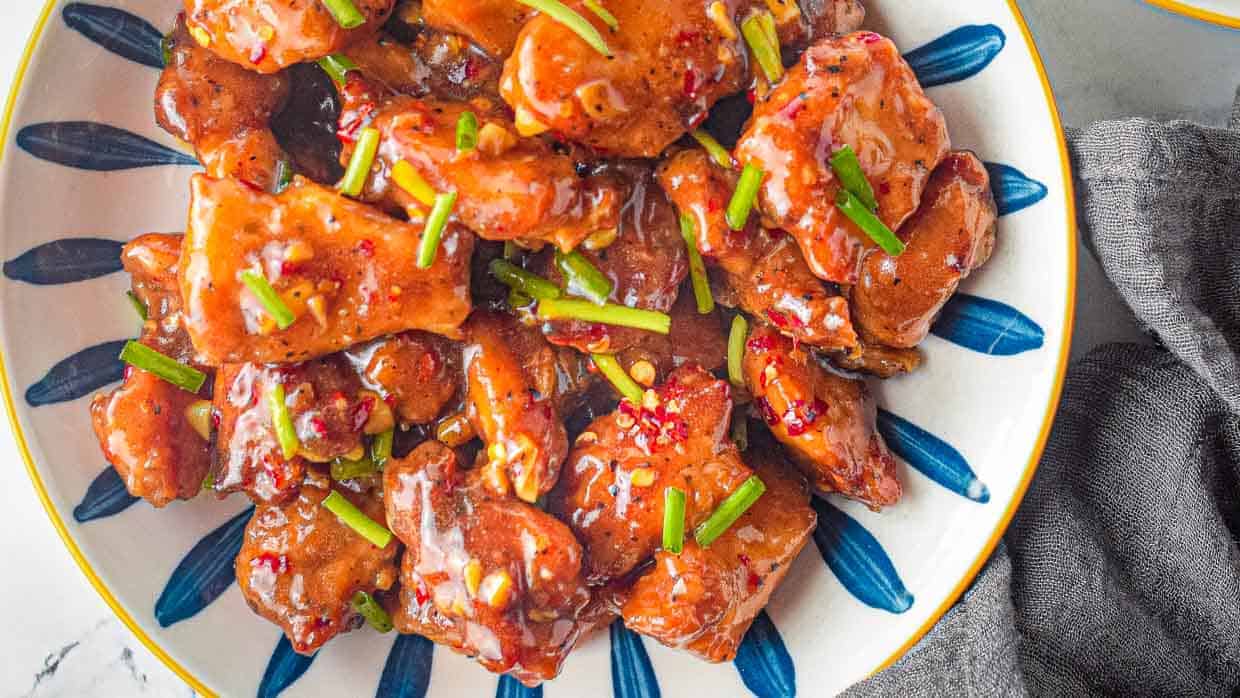 Honey garlic chicken with green onions on a blue and white plate.