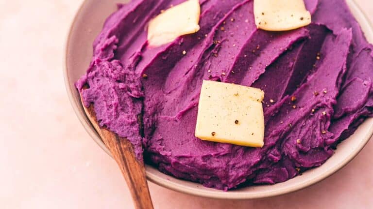 Purple sweet potato puree in a bowl with a wooden spoon.