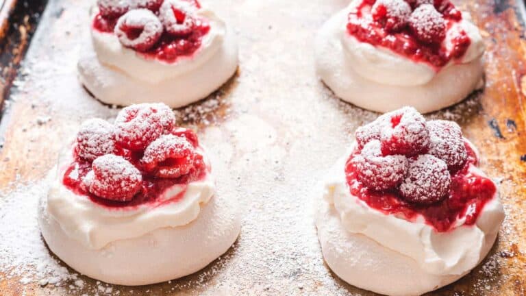 Pavlovas with raspberries and powdered sugar on a baking sheet.