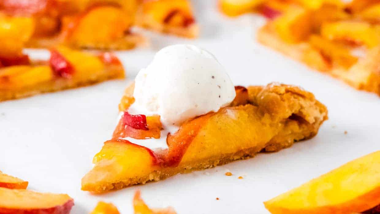 Piece of peach crostata topped with vanilla ice cream.