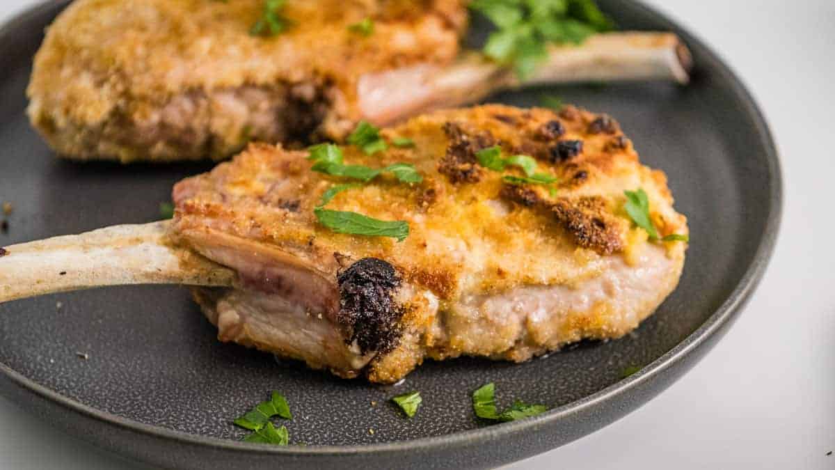 Two breaded pork chops on a gray plate with parsley.