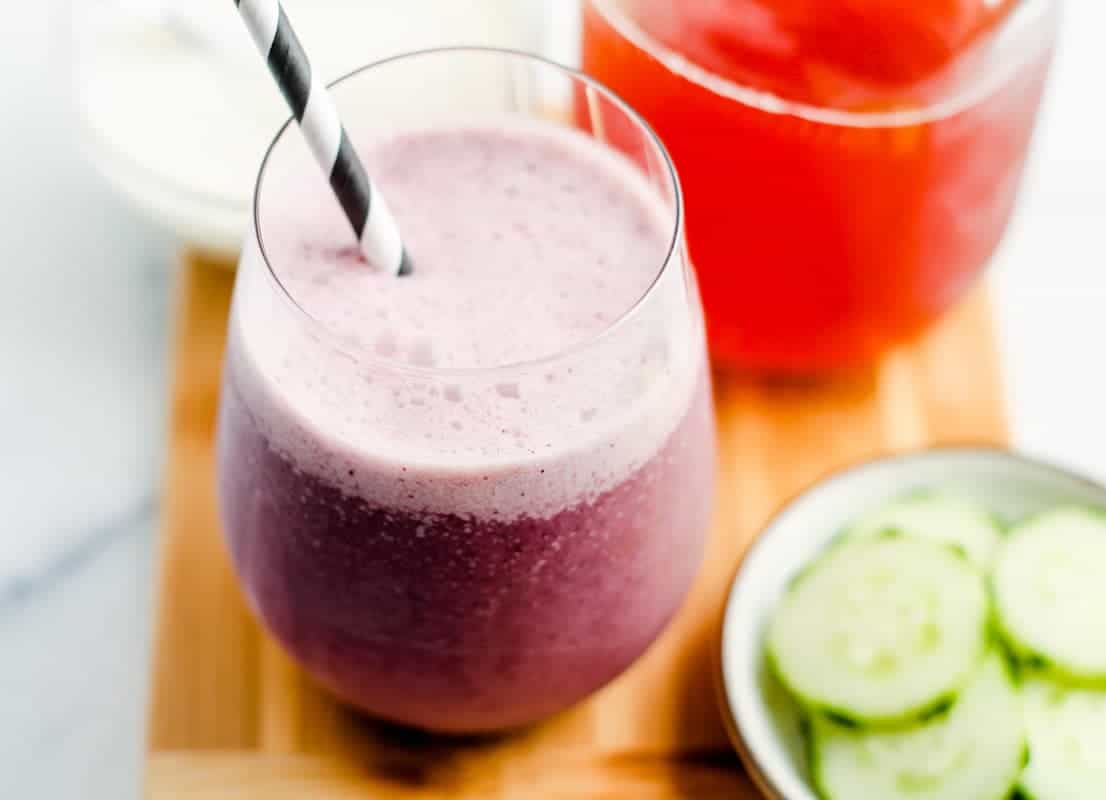 A glass of probioitc smoothie on a counter with a jar of kombucha behind it.