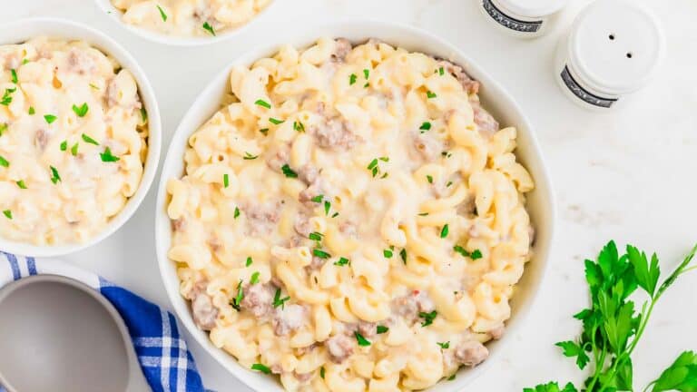 A bowl of macaroni and cheese with sausage and parsley.