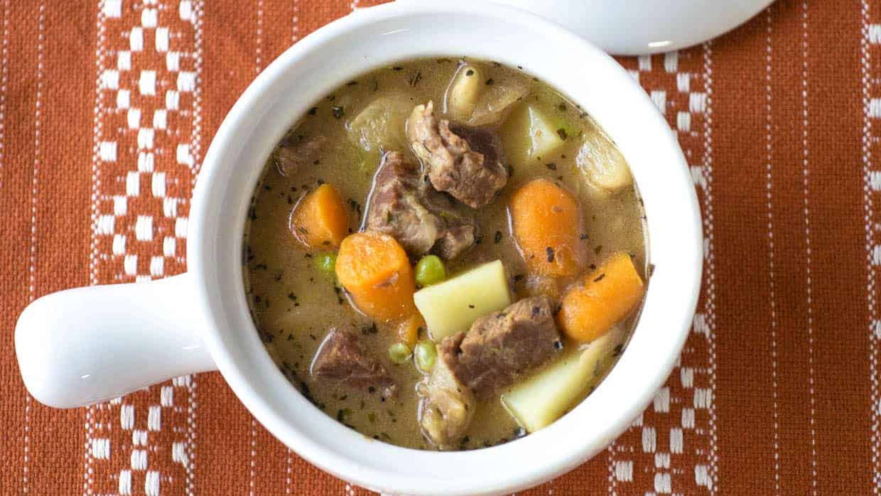 Top view of a bowl of beef stew with carrots, potatoes and peas.