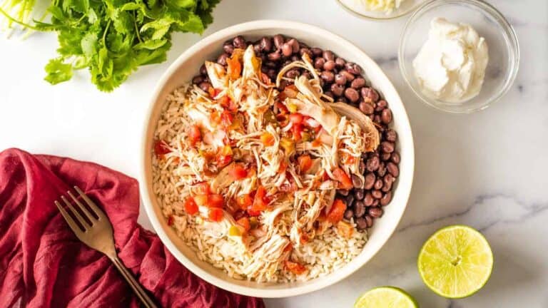 Mexican chicken rice in a white bowl with limes and black beans.