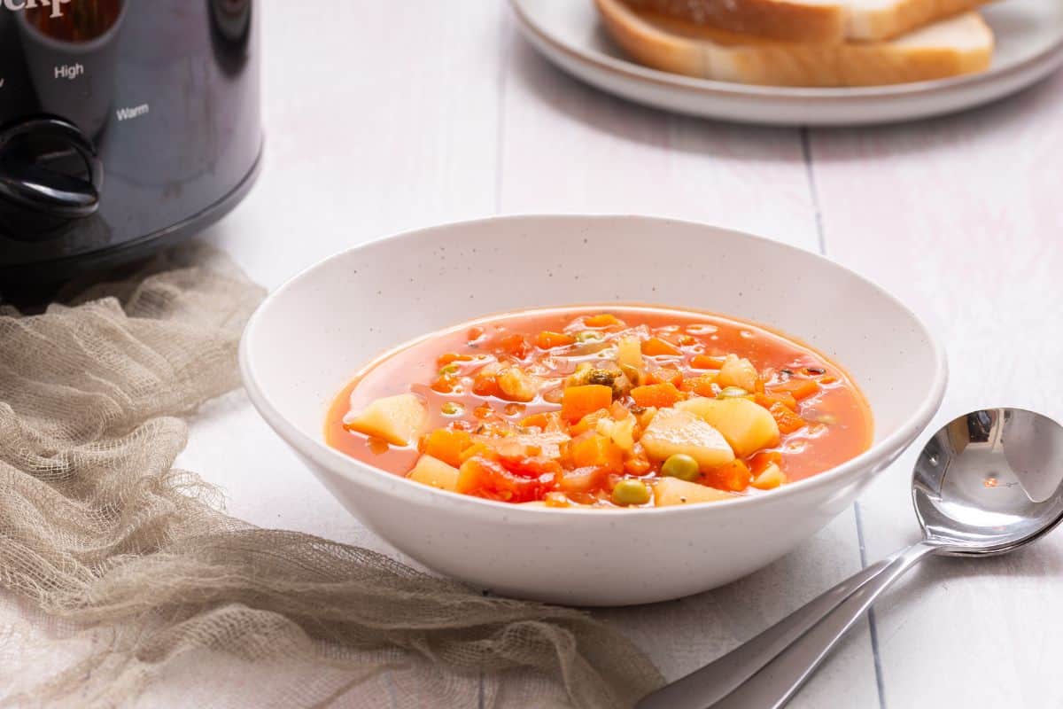 A bowl of soup in front of a slow cooker.