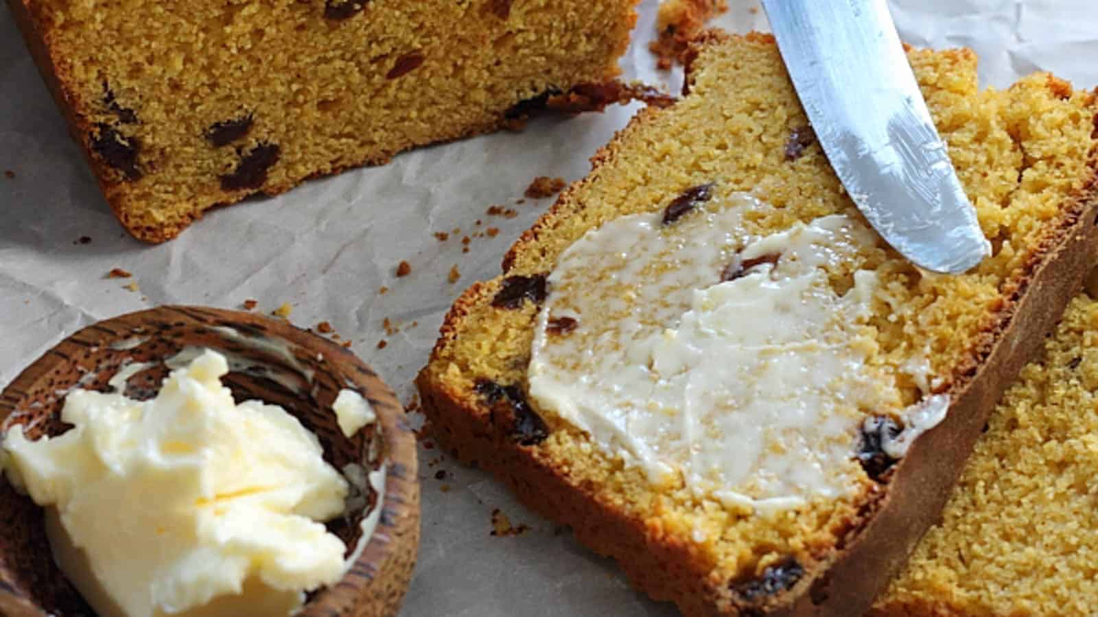 Slice of sweet potato raisin bread with butter spread and small bowl of butter to the side.