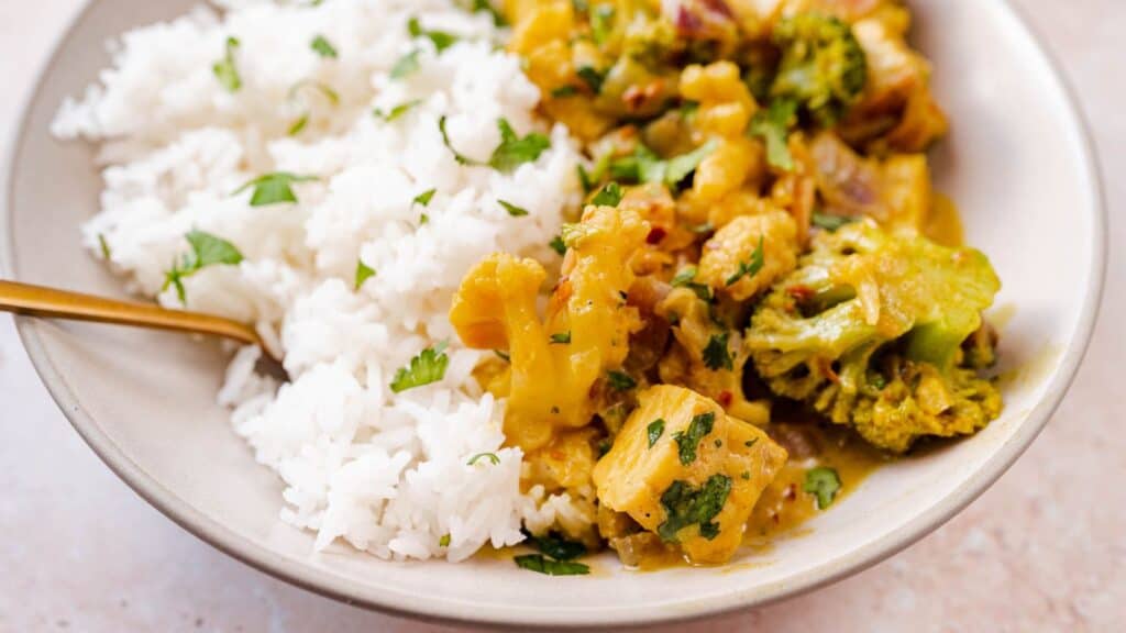 A bowl of chicken curry with rice and broccoli.