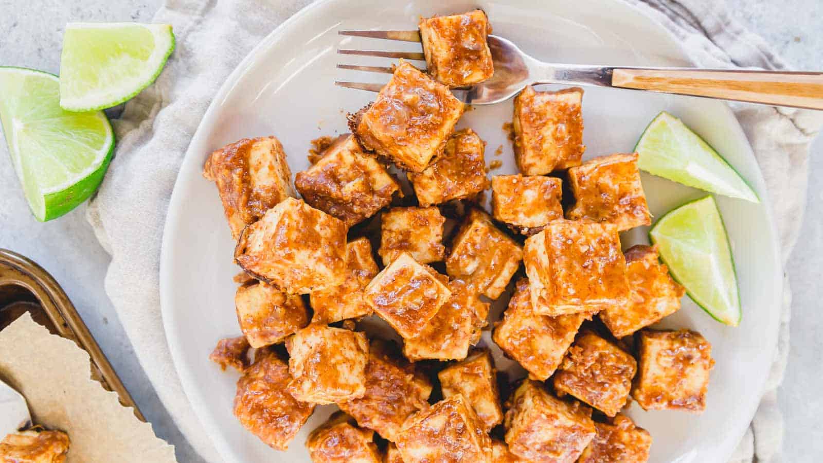 Tofu on a plate with lime wedges and a fork.