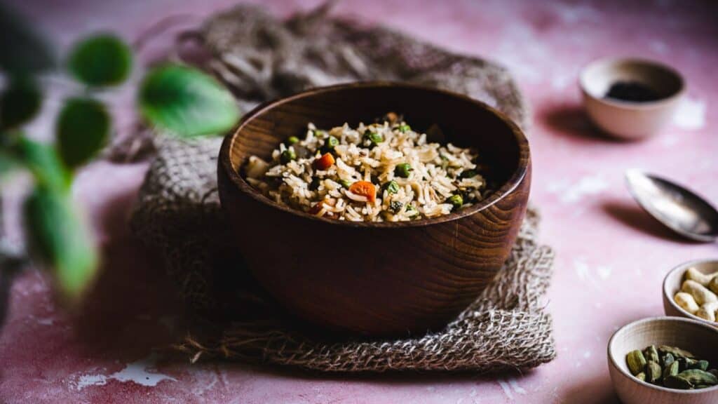 Rice in a wooden bowl on a pink background.